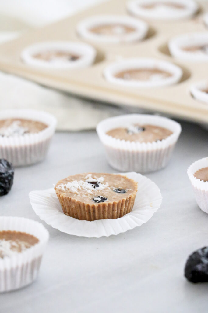 Vertical photo with prune cups inside muffin pan and on the counter.