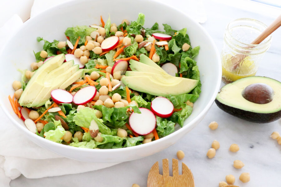 Salad bowl in center / left side. Utensils on the right side with half of avocado.