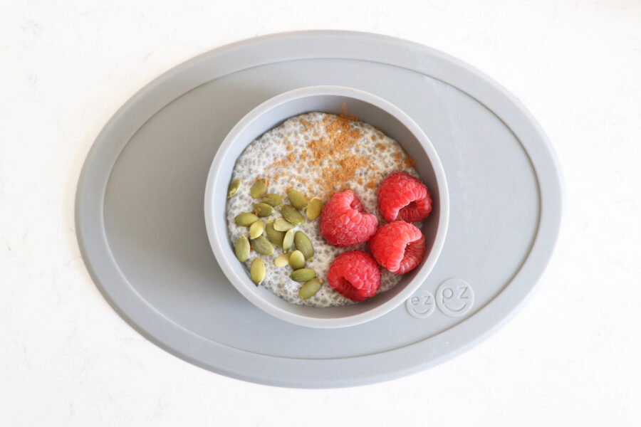 Grey bowl with chia pudding, pumpkin seeds and raspberries.