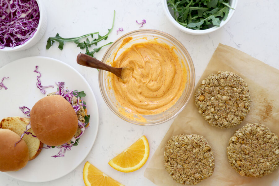 Baked burgers on the bottom right, bowl of buffalo sauce in the middle and full burgers on the left side.