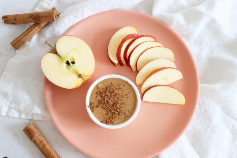 Pink plate with sliced apples and nut butter topped with cinnamon.