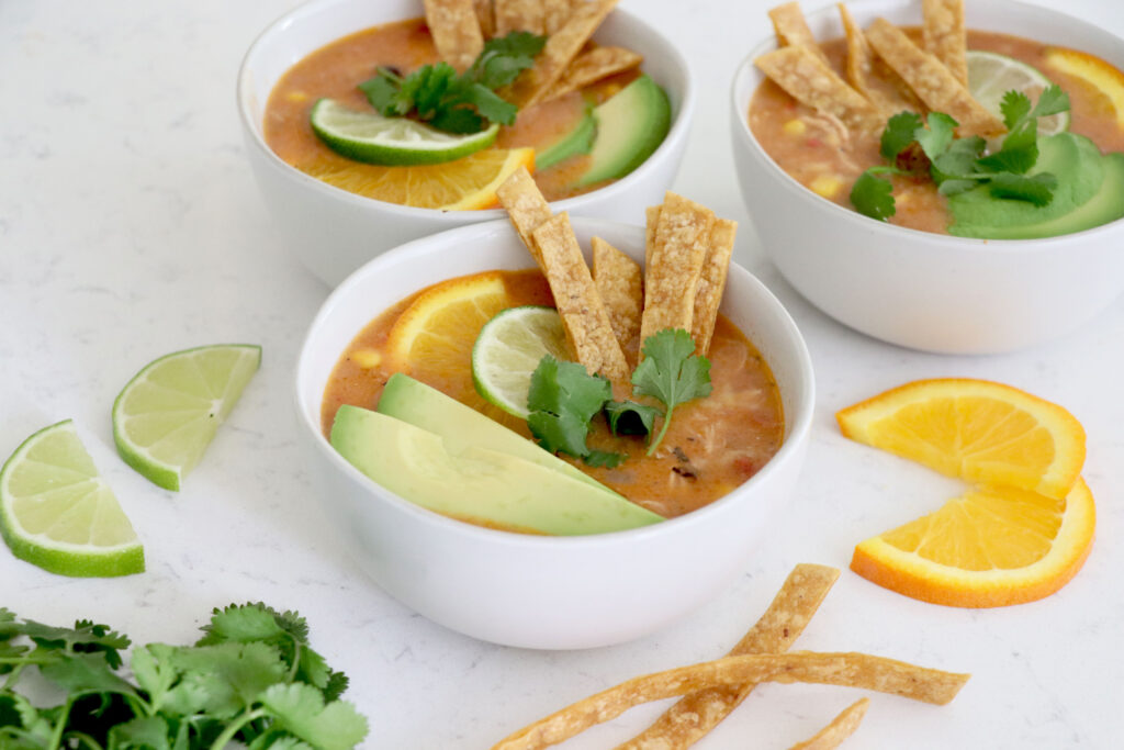 Three white bowls with nacho soup topped with tortilla strips and sliced avocado.