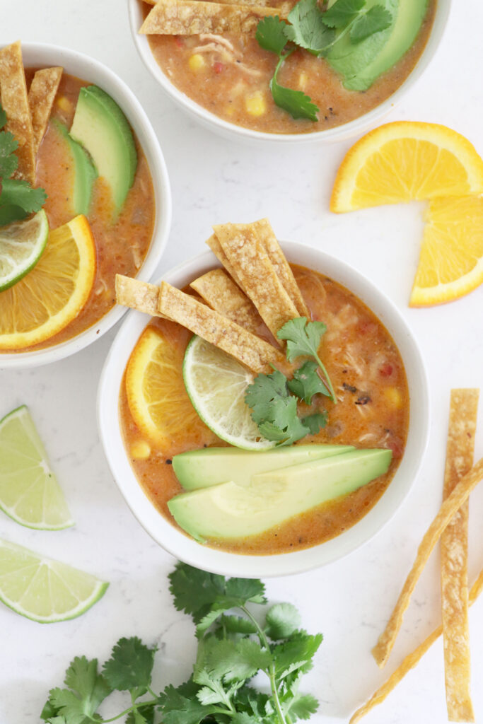 three bowls of citrus nacho soup topped with tortilla strips, avocado slices and citrus.
