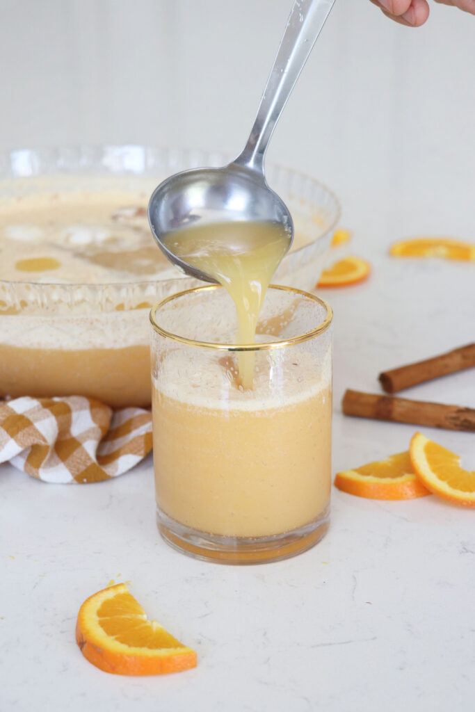 Glass bowl of citrus punch and ladle pouring punch into glass.