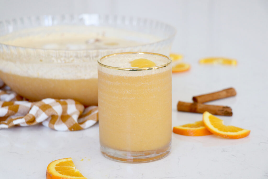 Glass of citrus cider with punch bowl behind glass.