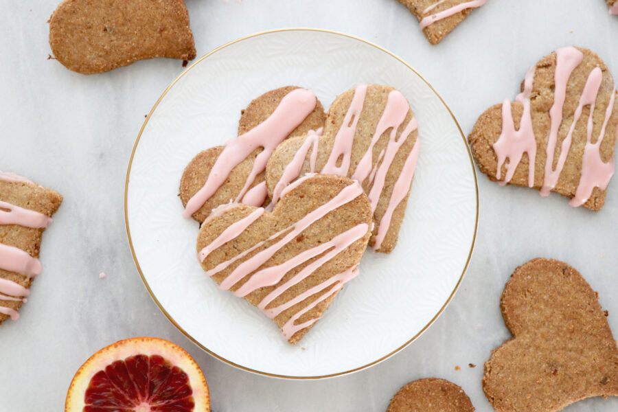 Heart shaped cookies with pink icing on top. Slice of blood orange in background.