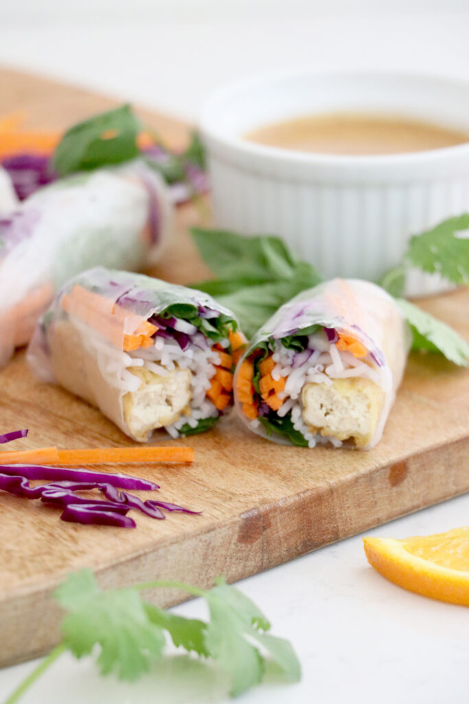Wooden cutting board with veggie spring roll cut in half.