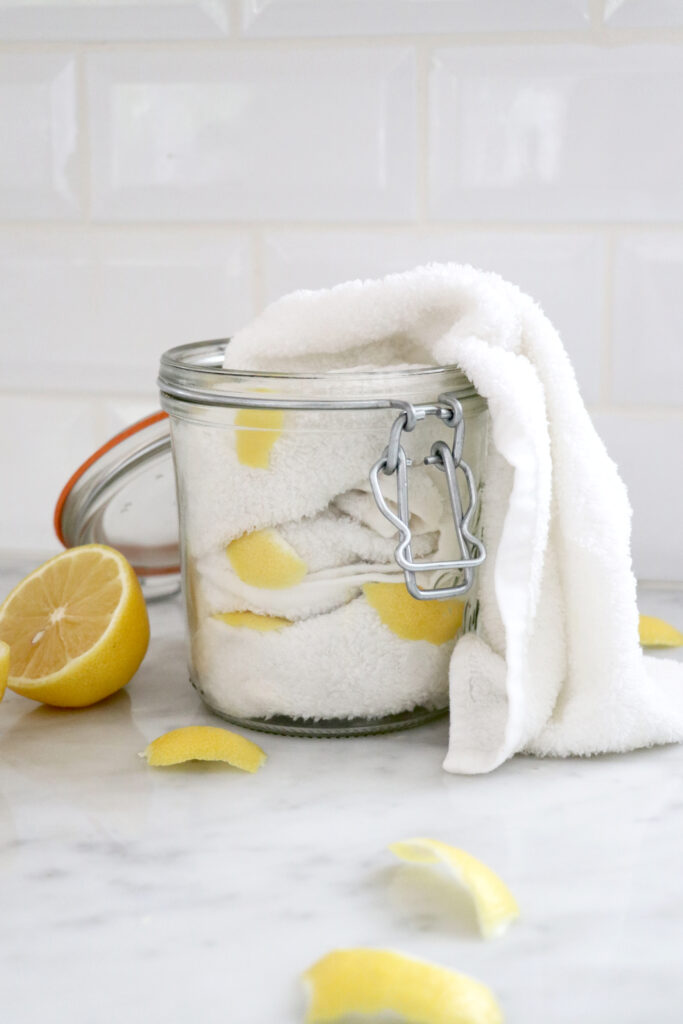 Glass jar filled with white towels and lemon slices with lemon on the side.