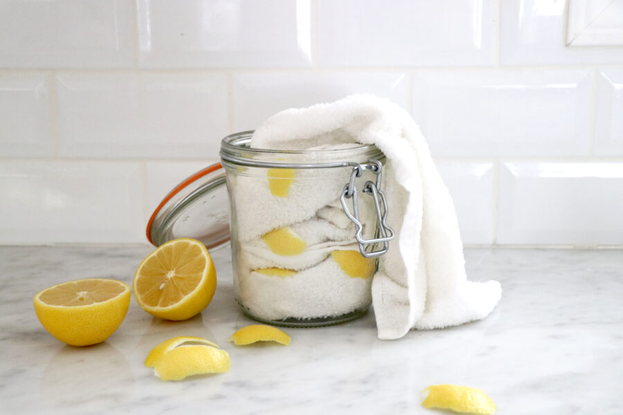 Glass jar filled with white towels and lemon slices with lemon on the side.