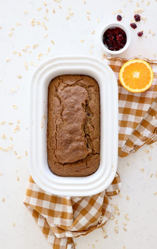 Bread pan with blender bread on top with brown and white checkered towel. Orange slice on the side.