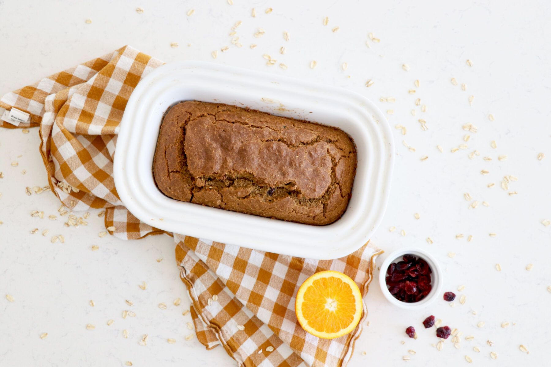 Bread in white bread pan on top of checkered towel.