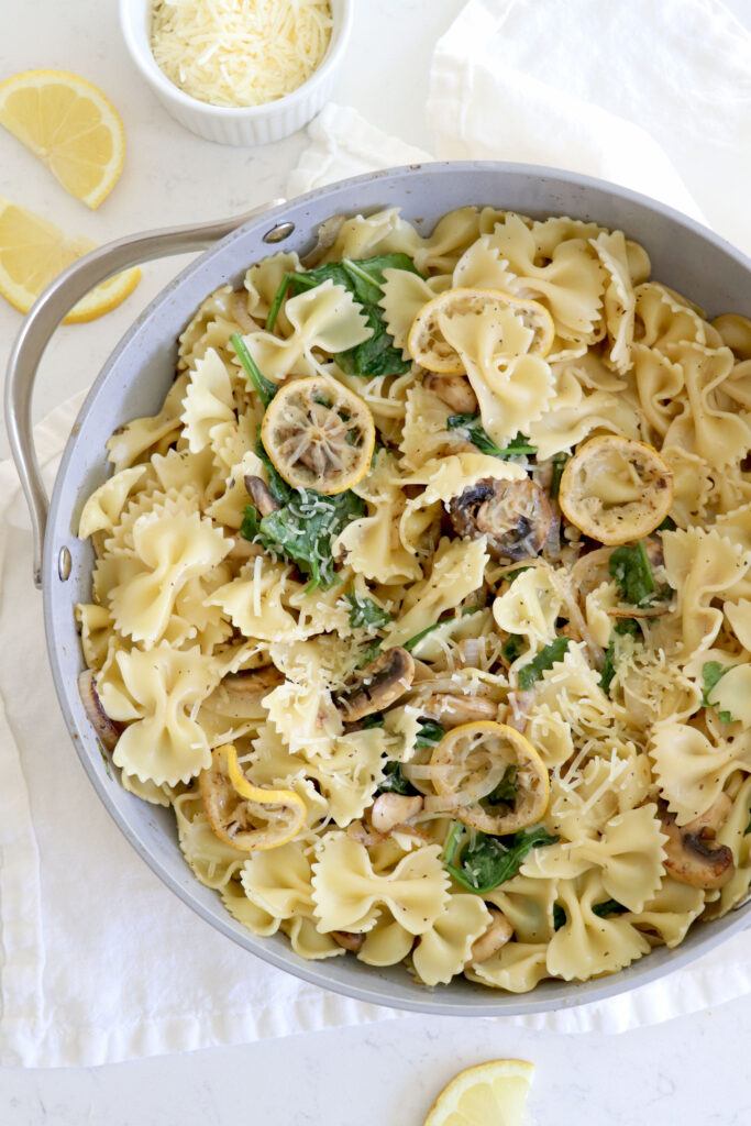 large saucepan with creamy lemon bowtie pasta and veggies like spinach and mushrooms.