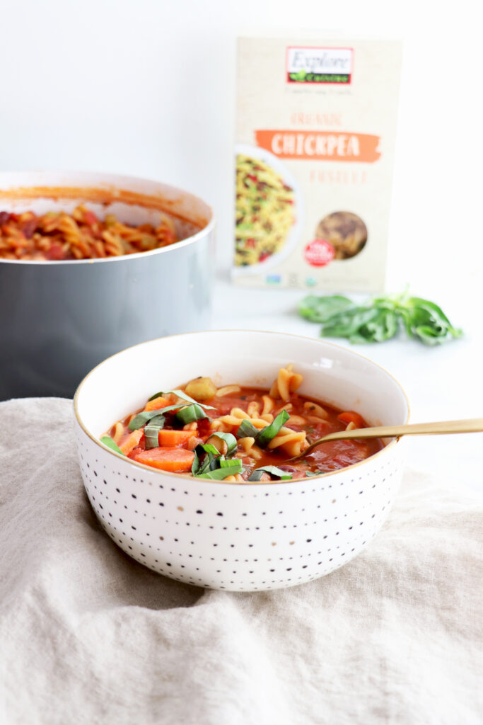 Bowl of minestrone soup with pot of minestrone soup in the background and box of noodles to the side