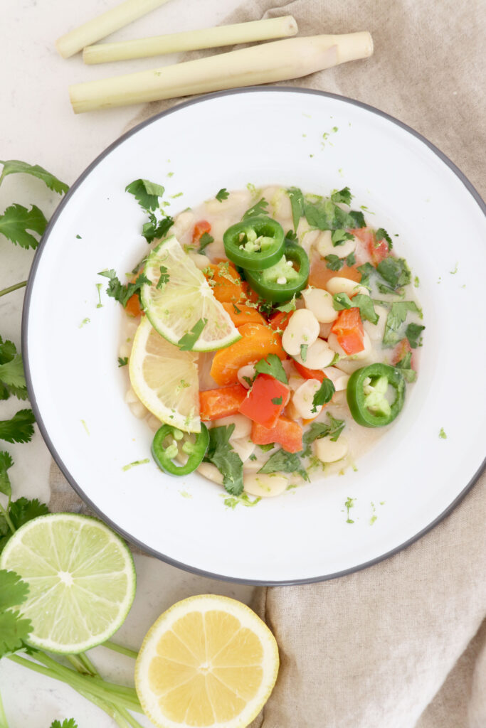 White bowl with soup and lime and lemon slices on the side.