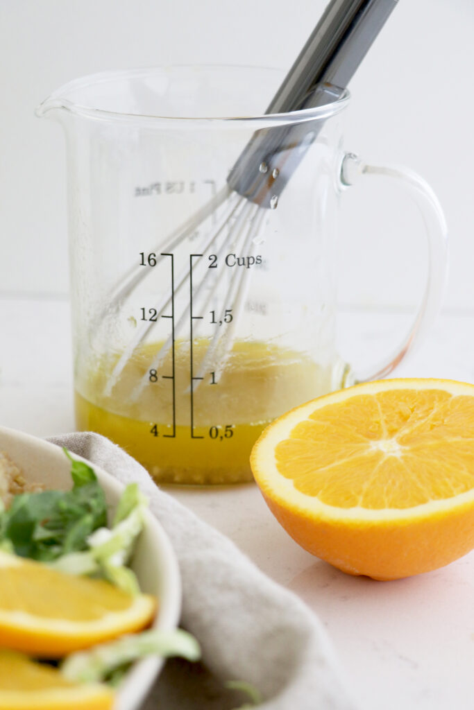 Measuring cup with orange dressing and half an orange on the side.
