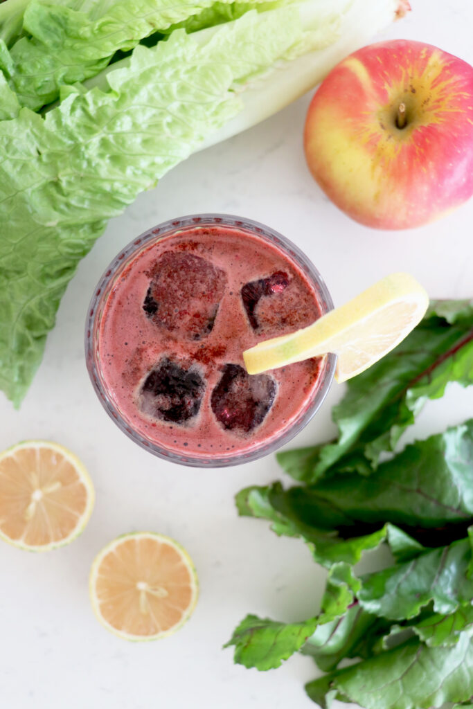 Birds eye view of glass with beet juice surrounded by fruits and veggies.