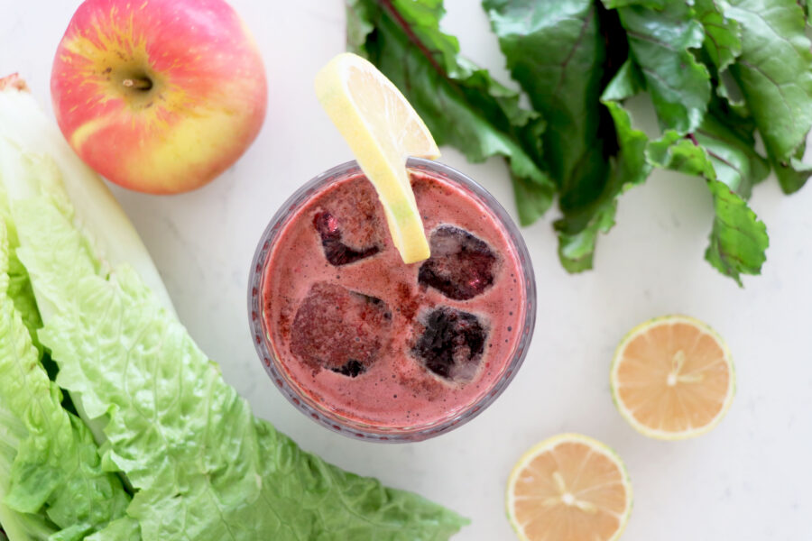 Glass of beet juice surrounded by fruits and veggies.