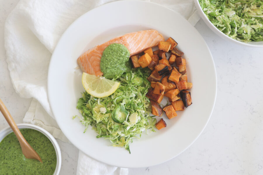 White plate with salmon, sweet potatoes and broccoli pesto.