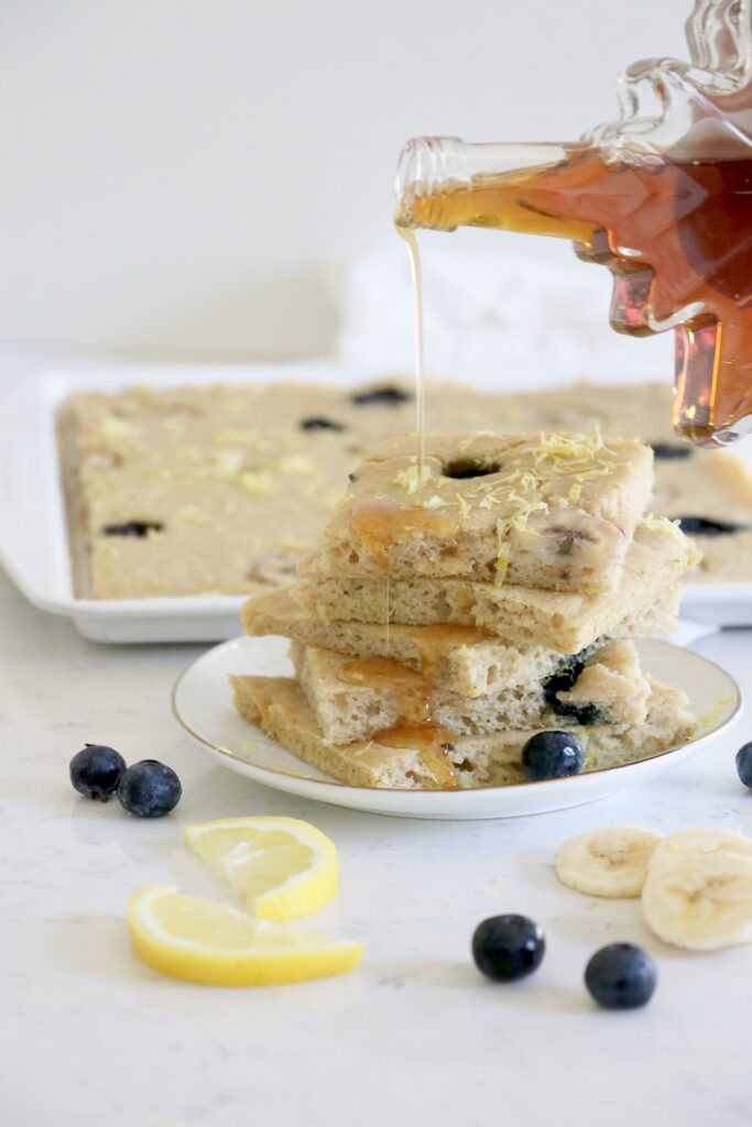 Sheet pan with pancakes and white plate in front with square pancakes topped with maple syrup.