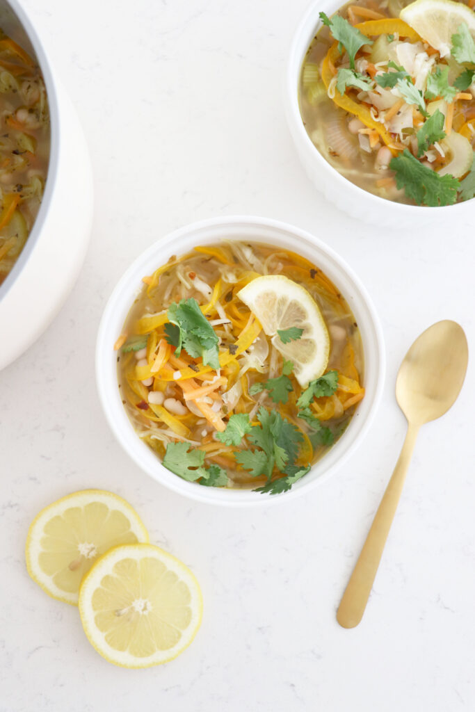 Two white bowls with cabbage soup, spoon on the side and 2 lemon slices.