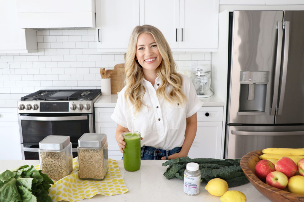 Megan holding green drink with vitamins and plant-based foods on counter.