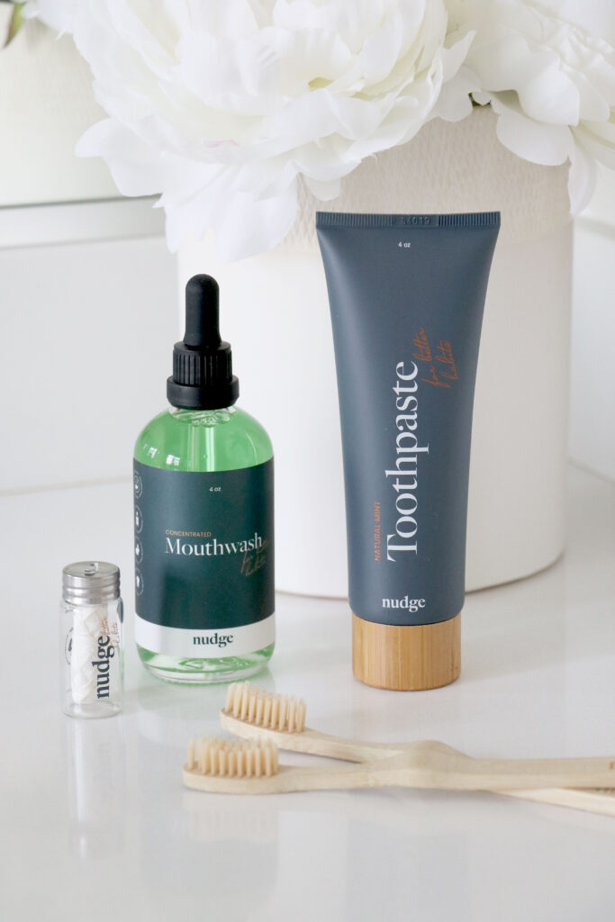 Natural Flouride Free Toothepaste From Nudge on Countertop with mouthwash, toothbrush, detanl floss and vase of flowers