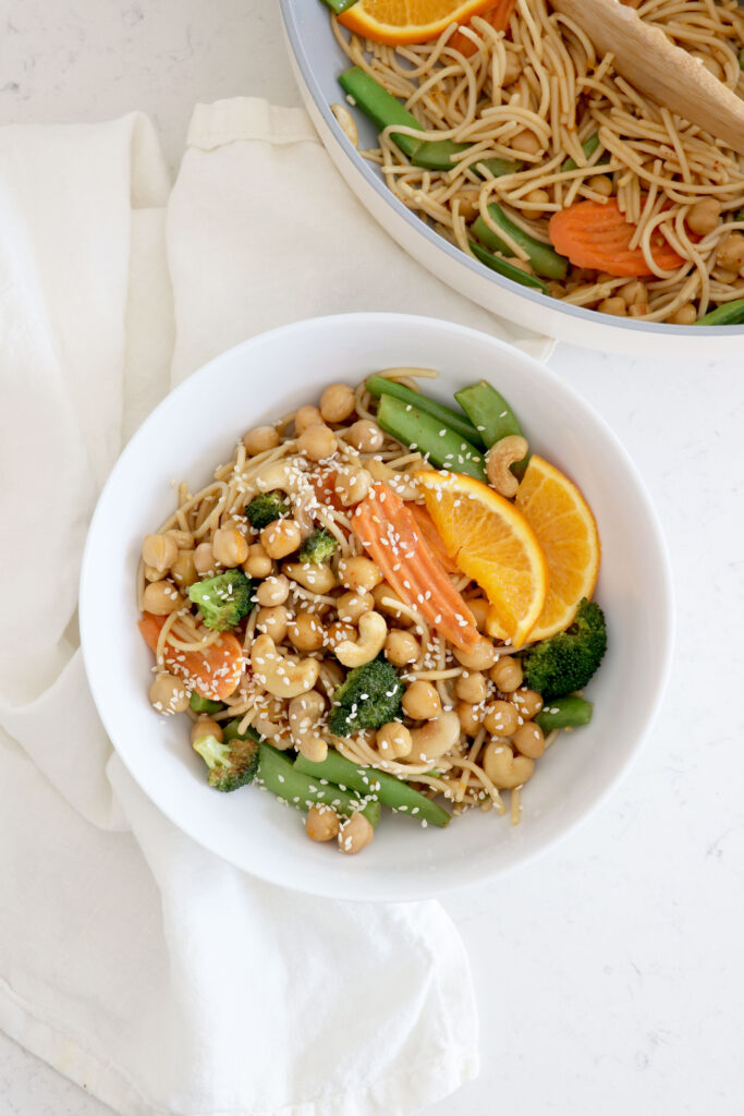 Saucepan with chow mein in top right corner and white bowl of chow mien in center.
