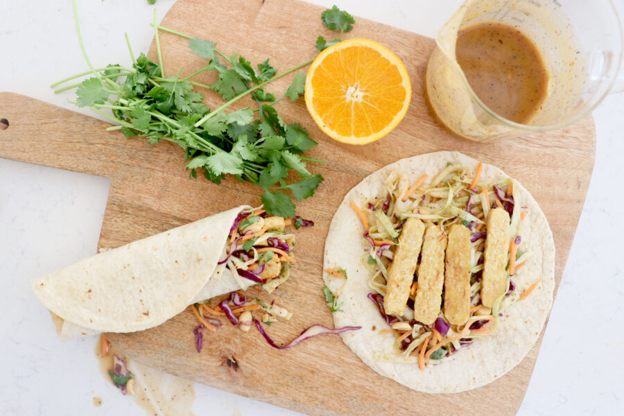 Wooden board with tempeh peanut wraps, sliced orange and cilantro.