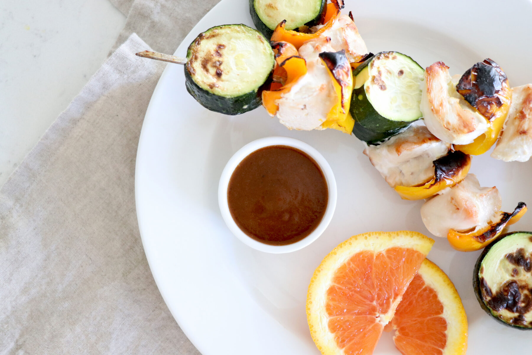 White plate with two skewers and cup of bbq sauce with orange slices on the side of plate.