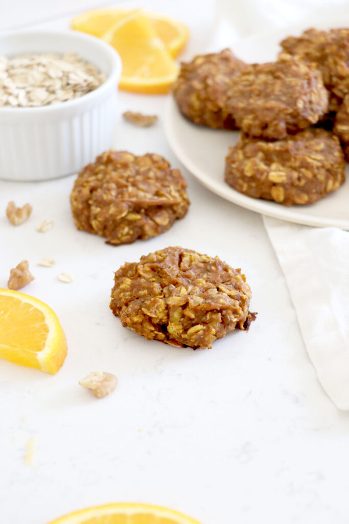 Pumpkin cookies on table and white plate with orange slices surrounding.