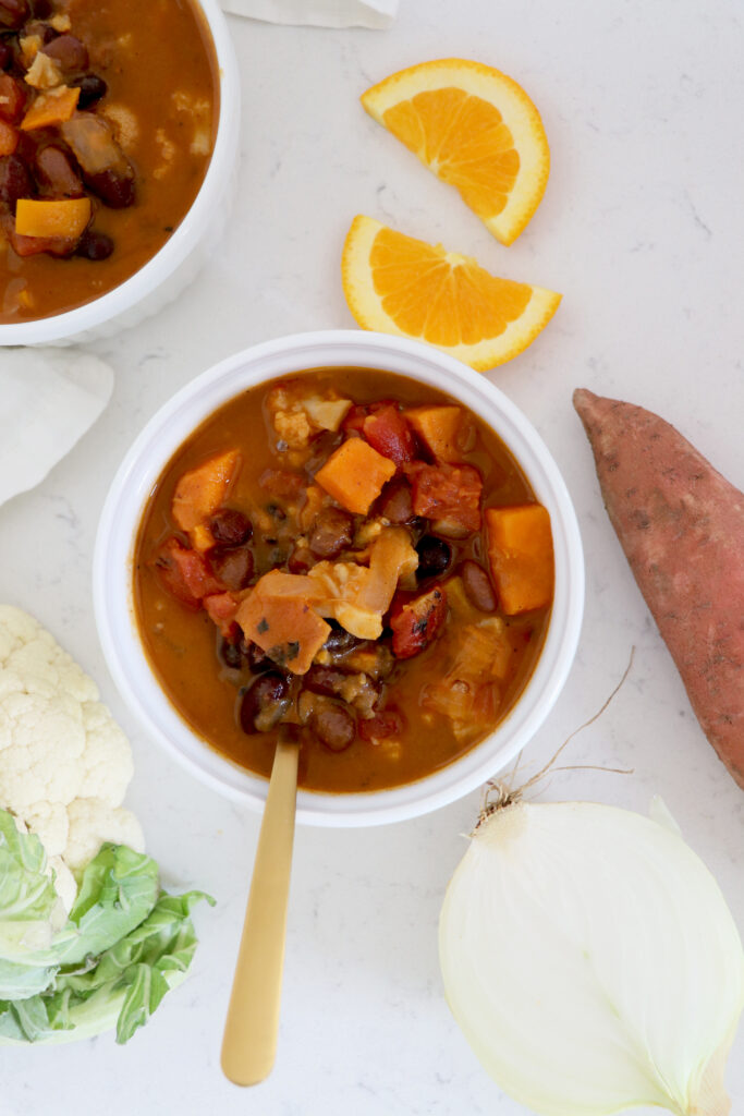 Bowl of chili with gold spoon and orange slices and sweet potato.