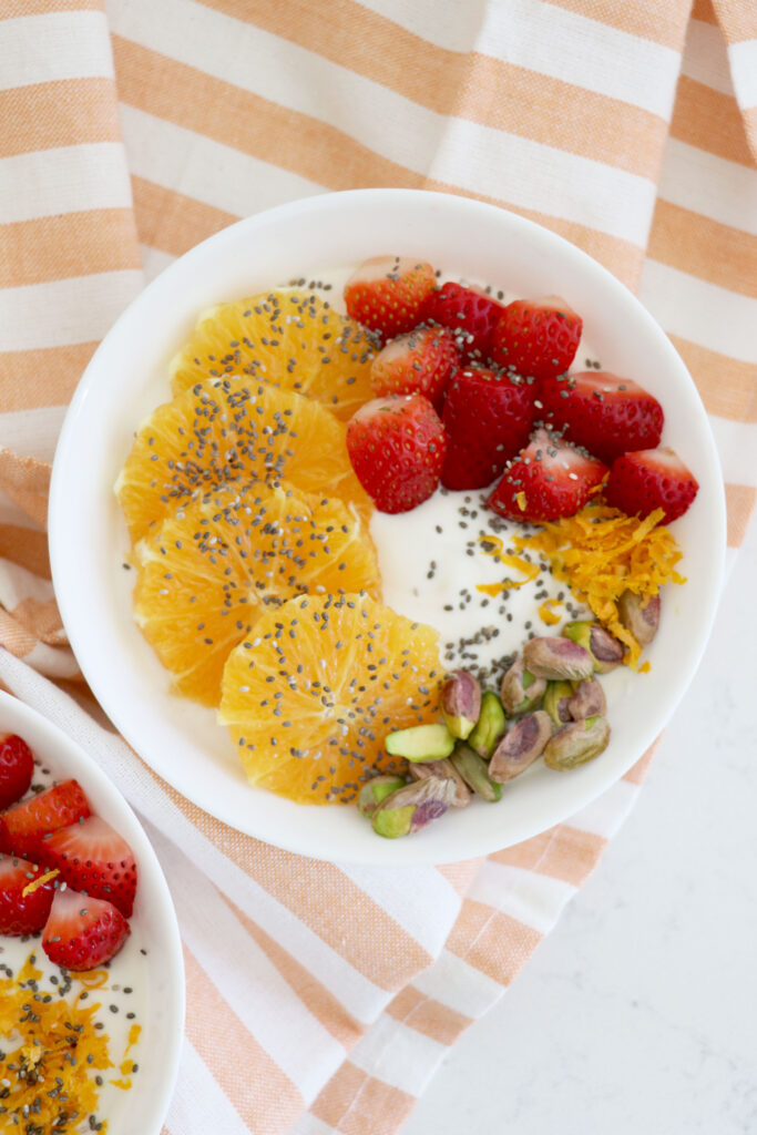 Striped napkin with white yogurt bowl on top with orange slices and strawberry slices.