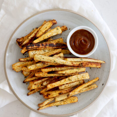 Parsnip fries on white plate with a small dish of ketchup