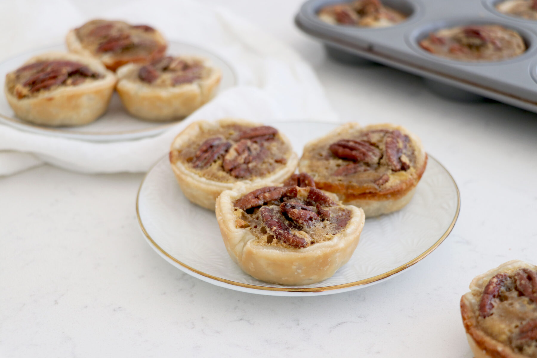 Two plates with 3 mini pies on each and pie pan on top right.