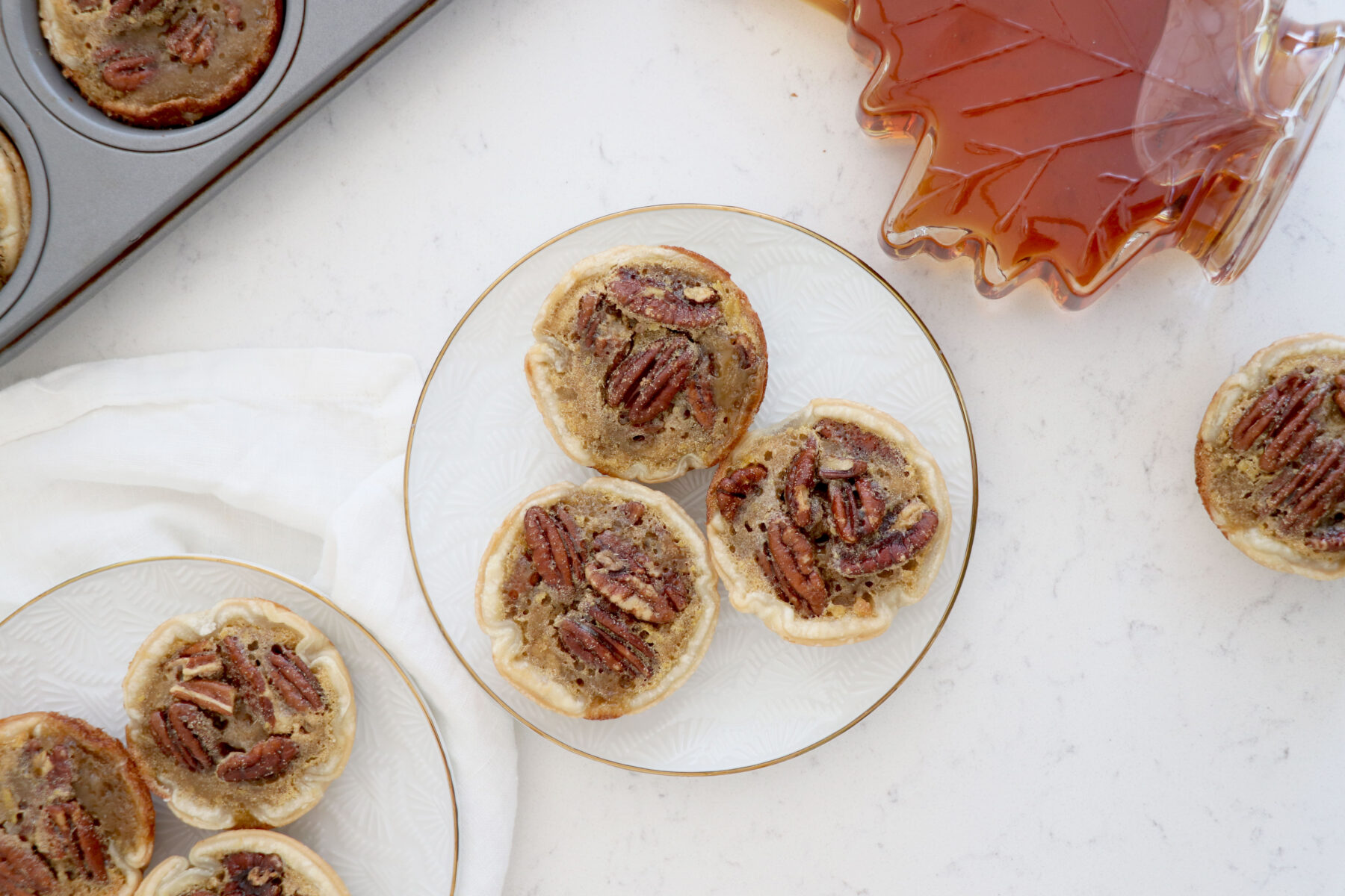 Two plates with 3 mini pies and maple syrup on top right.