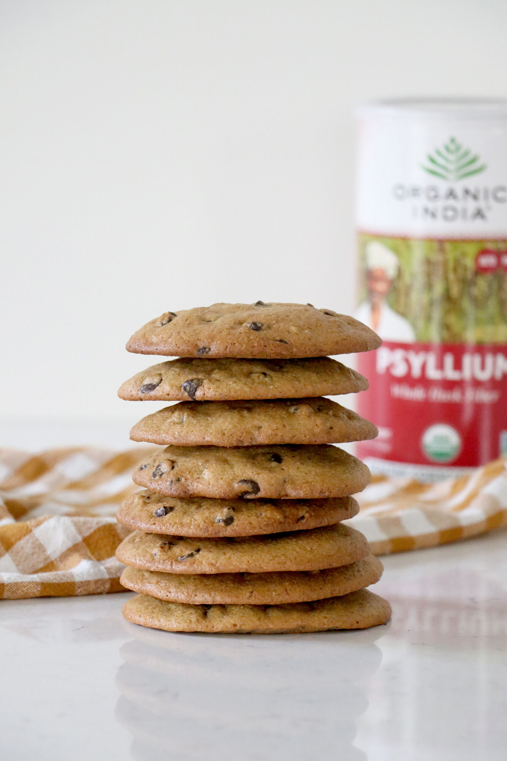 A stack of chocolate chip cookies on a kitchen counter with psyllium husk container in the background
