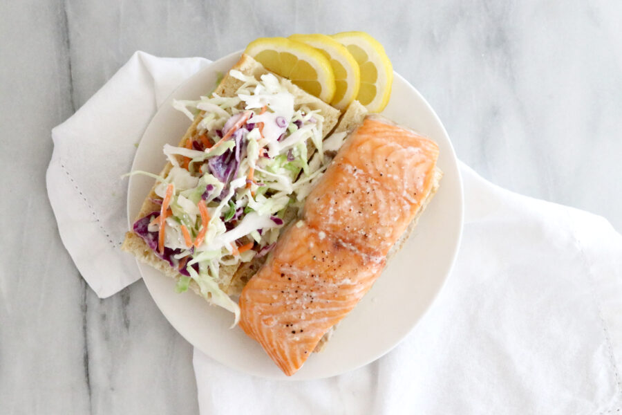 Salmon sandwich on white plate in center of photo sitting on top of a white napkin.