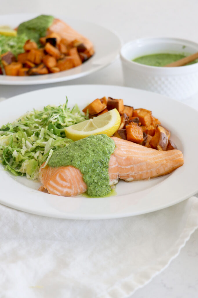 White plate with baked salmon and pesto with Brussels salad.