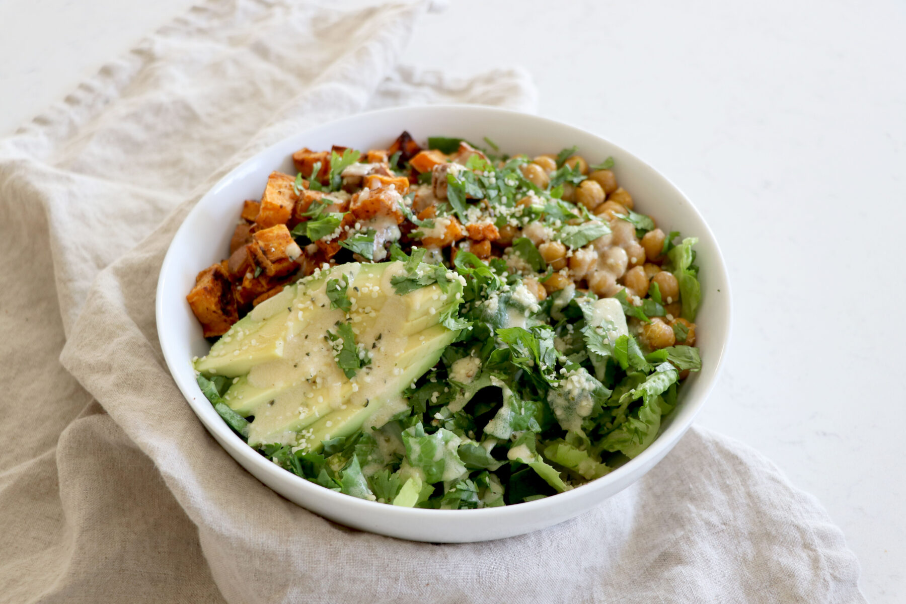 Large salad topped with avocado, sweet potato, chickpea and lemon tahini dressing
