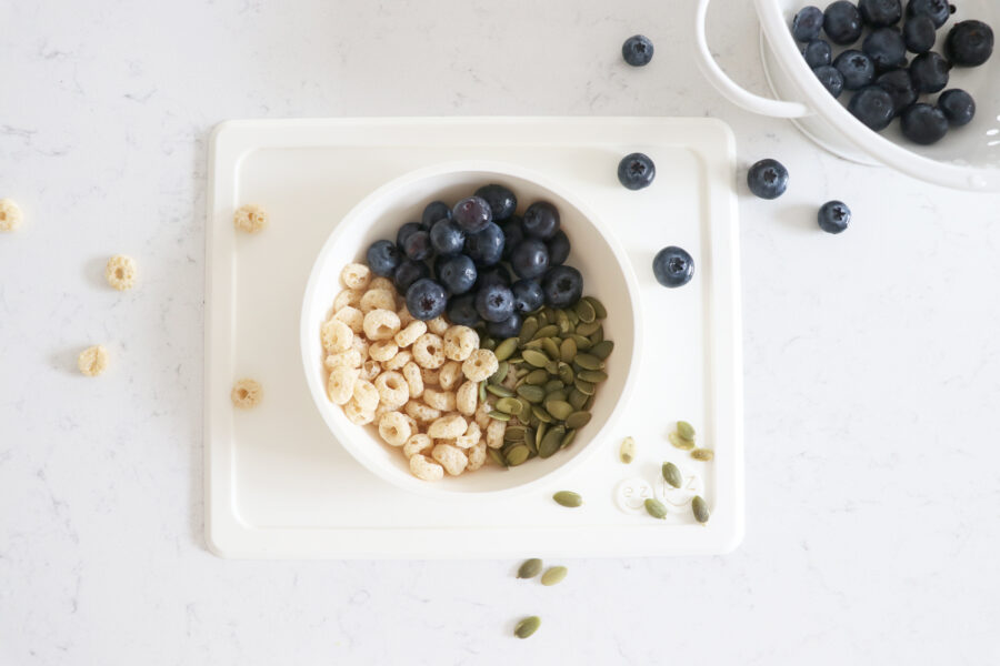 White bowl with blueberries, pumpkin seeds and cereal.