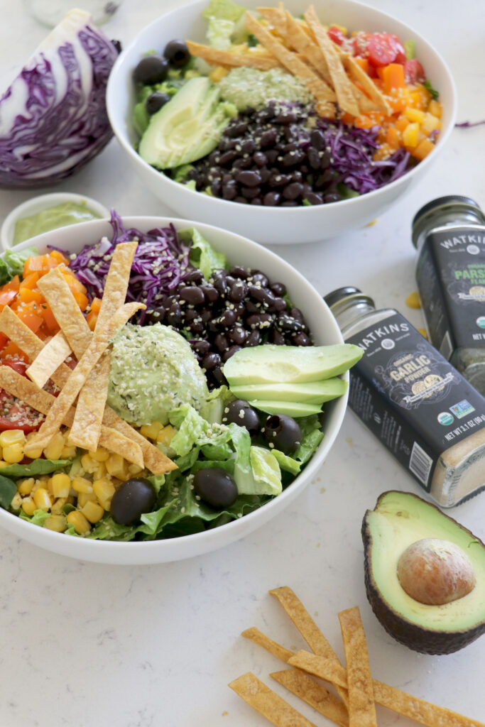 Two bowls of taco salad with avocado and seasoning on the side.